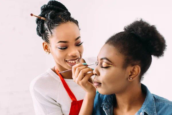 Young beautiful African American woman applying professional make-up by African make-up artist. Studio shoot — Stock Photo, Image