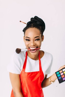 Güzel genç Afro-Amerikan güzellik kadını beyaz izole, fırçalar ve göz farları makyaj seti tutan