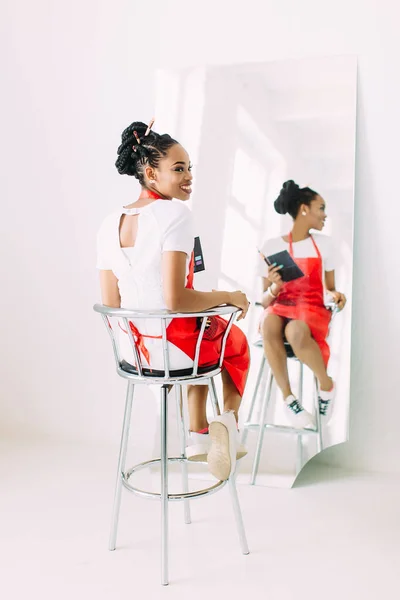 Vacker ung afrikansk amerikansk kosmetolog kvinna innehav uppsättning sminkborstar och tittar i spegeln — Stockfoto