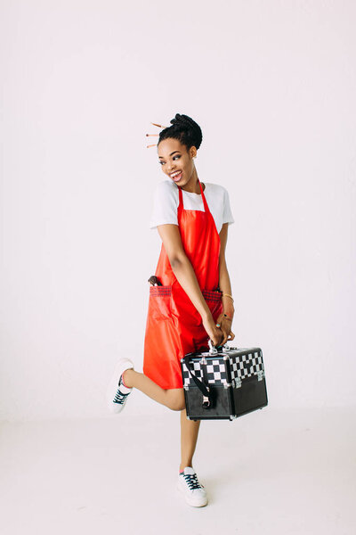 Красивая молодая афро-американская косметолог держит набор косметического оборудования в специальном случае, изолированные на белом фоне
