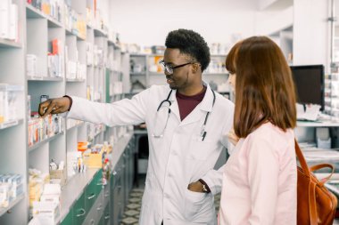 Afrikalı gülümseyen neşeli olumlu mutlu adam eczacı eczacı genç kadın müşteri için tıp tavsiye ediyor.