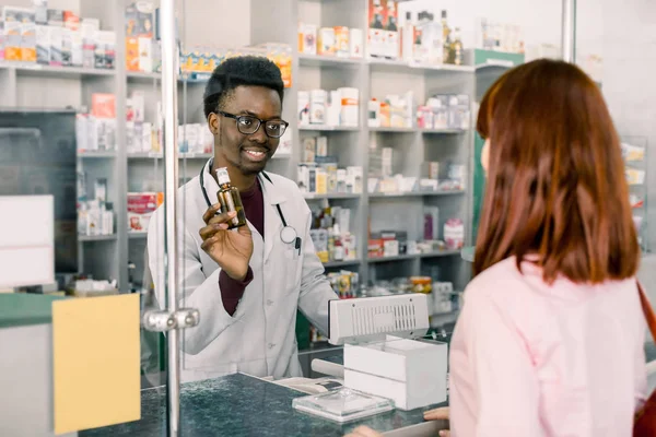 Lékařství, farmaceutik, zdravotnictví a lidé-spokojený mladý Afričan, lékárník, který dává léky mladé krásné ženě v lékáčnictví — Stock fotografie