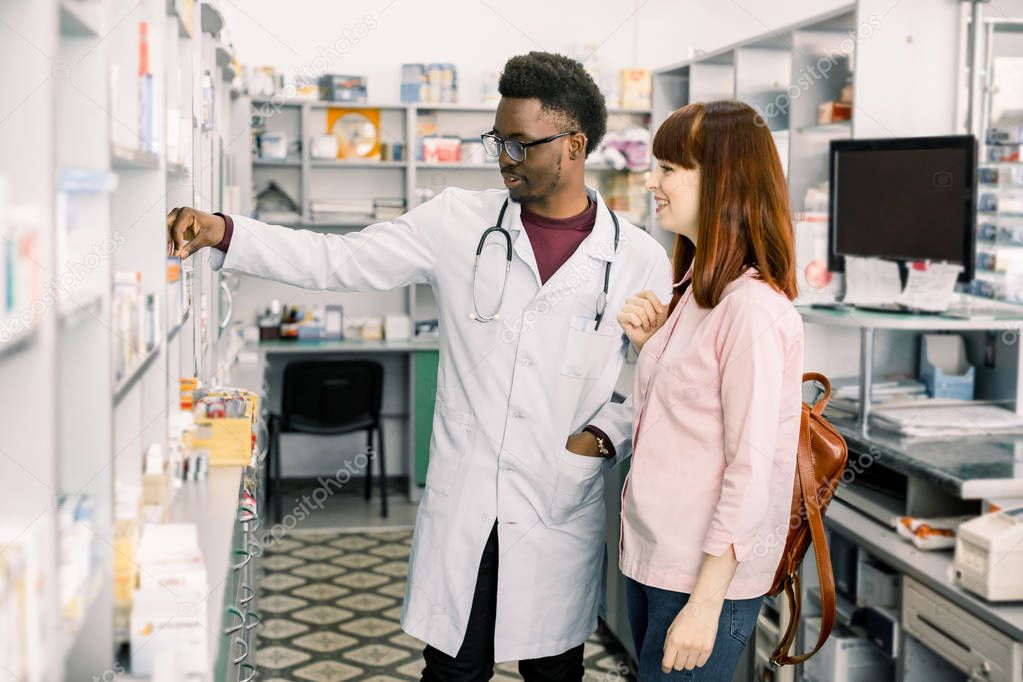 Experienced African American man pharmacist consulting female customer in modern pharmacy