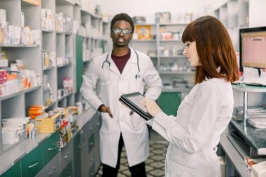 İki genç neşeli Eczacılar Afrikalı adam ve beyaz kadın birlikte çalışıyor. Kadın tablet kullanıyor. Eczaneler hastane eczanede reçete ile ilaçlar arama