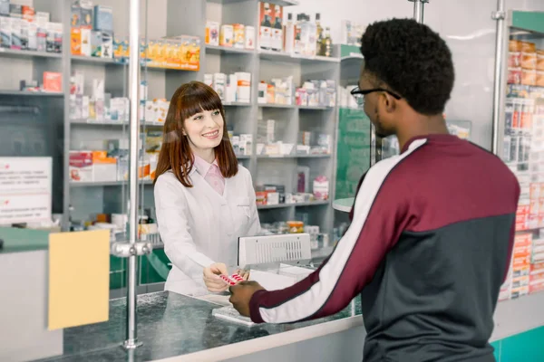 약국의 페이 데스크에 서 남성 아프리카 클라이언트에 약물을 주는 젊은 여자 약사 — 스톡 사진