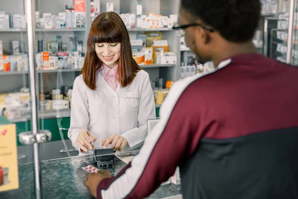 아프리카 남자 고객 약국에서 지불. 단말기를 들고 있는 약사 여성, 신용카드로 약용을 지불하는 남자. — 스톡 사진