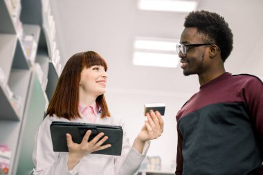 Mutlu Afrikalı adam müşteri modern eczane gerekli ilaçlar bulundu. Modern eczanede pozitif genç kadın eczacı sunan ilaç