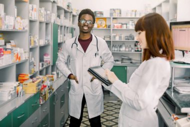 İki genç neşeli Eczacılar Afrikalı adam ve beyaz kadın birlikte çalışıyor. Kadın tablet kullanıyor. Eczaneler hastane eczanede reçete ile ilaçlar arama