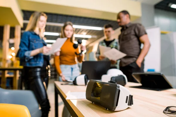 Imagen borrosa de cinco personas de negocios multiétnicos están desarrollando un proyecto utilizando aparatos modernos y gafas de realidad virtual. Concéntrate en las gafas VR sobre la mesa. tecnologías del futuro —  Fotos de Stock