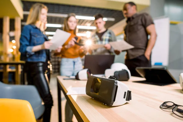 Imagen borrosa de cinco personas de negocios multiétnicos están desarrollando un proyecto utilizando aparatos modernos y gafas de realidad virtual. Concéntrate en las gafas VR sobre la mesa. tecnologías del futuro —  Fotos de Stock