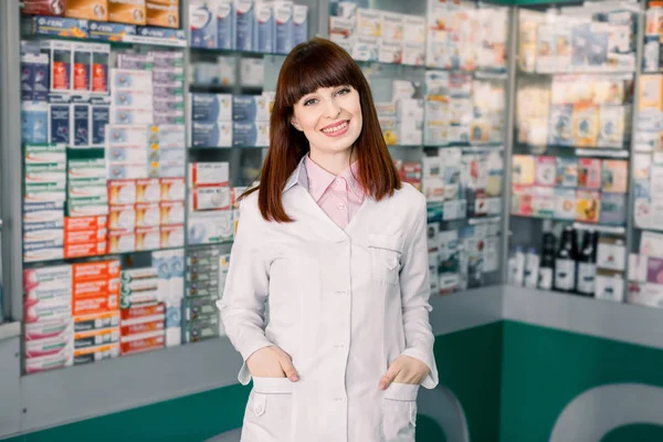 Medicine, pharmaceutics, healthcare and people concept. Portrait of a happy female pharmacist. Cheerful pharmacist chemist woman standing in pharmacy drugstore