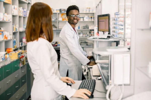 현대 약국에서 여성과 남성 약사, 서로 보고, 컴퓨터에서 작업 하는 동안 — 스톡 사진