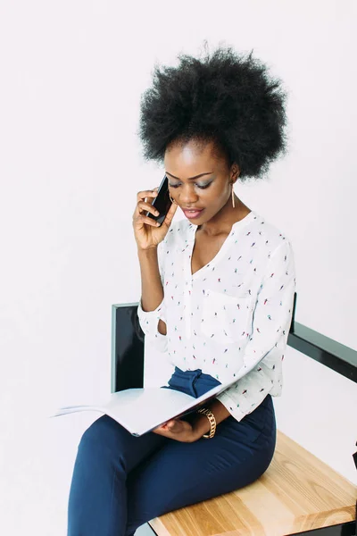 Vrolijke jonge Afro Amerikaanse zakelijke vrouw praten op mobiele telefoon, zittend op de stoel, geïsoleerd op wit — Stockfoto