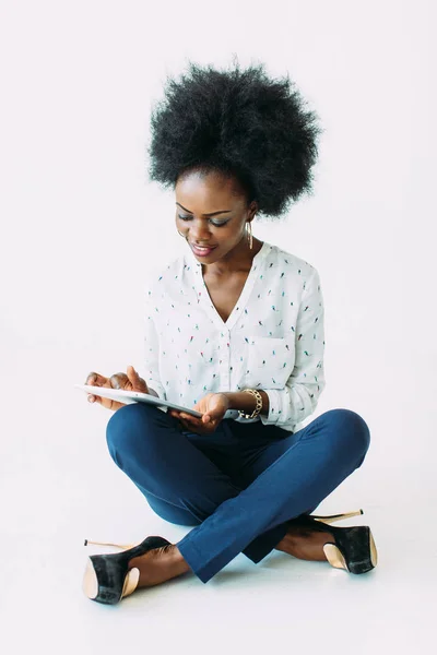 Jonge Afro-Amerikaanse zakenvrouw die de tablet gebruikt terwijl hij op de vloer zit, geïsoleerd op wit — Stockfoto