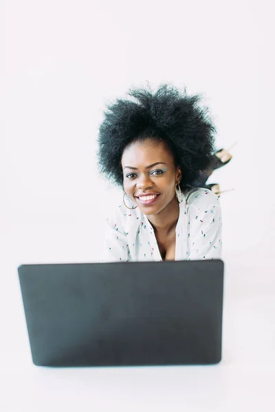 Giovane donna d'affari afroamericana che utilizza il computer portatile, sdraiata sul pavimento, isolata su sfondo bianco — Foto Stock
