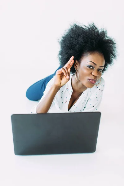 Giovane donna d'affari afroamericana che utilizza il computer portatile, sdraiata sul pavimento, isolata su sfondo bianco — Foto Stock