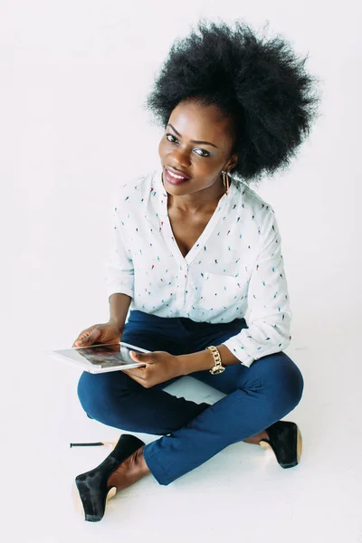 Giovane donna d'affari afroamericana che utilizza il tablet mentre è seduto sul pavimento, isolato su bianco — Foto Stock