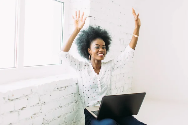 Giovane donna d'affari afro-americana sorridente che utilizza il computer portatile, seduta sul pavimento in uno studio di luce bianca — Foto Stock