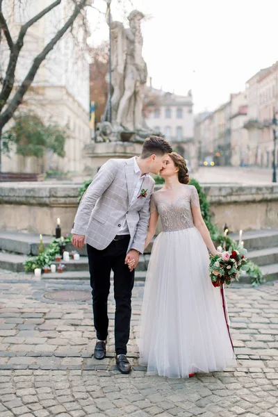 Romantická svatební dvojice v lásce, chůzi a líbání, drží se za ruce. Svatební výzdoba na kamenných schodech, památníku, Starodávné budovy na pozadí — Stock fotografie