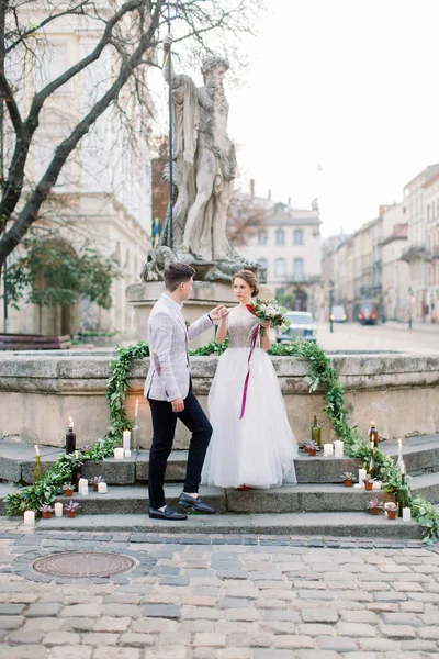 Sposa e sposo sulle scale monumento di pietra, passeggiata nuziale nella città vecchia. Cerimonia nuziale, decorata con candele, fiori e verde — Foto Stock