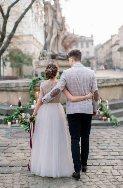 スタイリッシュなカップルの新郎新婦の背中の肖像画は、抱擁、リヴィウ、ウクライナの古代部分の記念碑の階段上の結婚式の装飾の前に立って — ストック写真