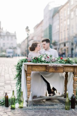 Romantik düğün çift şehir merkezinde mumlar, çiçekler ve sulu ile ahşap dekore masada oturan