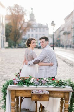 Romantik akşam yemeği mutlu düğün çift, dekore ahşap masada oturuyor. Arka planda inanılmaz eski Lviv mimarisi