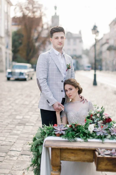 Sposo e sposa seduti al tavolo allestito per due nel centro storico della città. Matrimonio in stile rustico nella città del mattino — Foto Stock