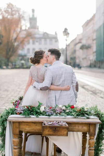 Felice coppia di nozze sulla cena romantica, seduto al tavolo di legno decorato. Incredibile vecchia architettura Leopoli su sfondo — Foto Stock