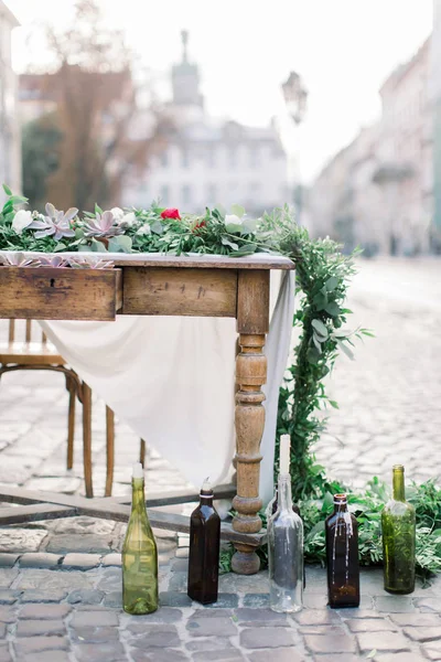 Wooden table and chairs decorated with flowers, succulents and decor. Glass bottles with candles. Decorated table on the stone pavement in Old City Lviv — Stock Photo, Image