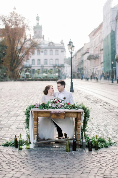 Romantik düğün çift şehir merkezinde mumlar, çiçekler ve sulu ile ahşap dekore masada oturan