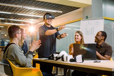 Vr gözlük giyen genç Çinli adam modern bir ofiste çok ırklı meslektaşları tarafından izlendi