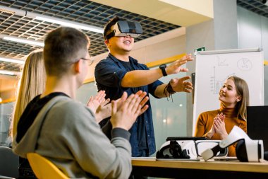 Sanal gerçeklik uygulamaları ve oyunları üzerinde çalışan çok ırklı kişilerden oluşan iş ekibi, vr gözlüklerini veya gözlüklerini test eden genç heyecanlı adam iş arkadaşlarıyla ofis odasında duruyor