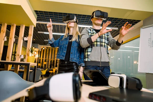 Ung leende man och kvinna i VR Goggles tittar på händer upphetsad med Augmented Reality. Par försöker VR glasögon och ha roligt inomhus — Stockfoto