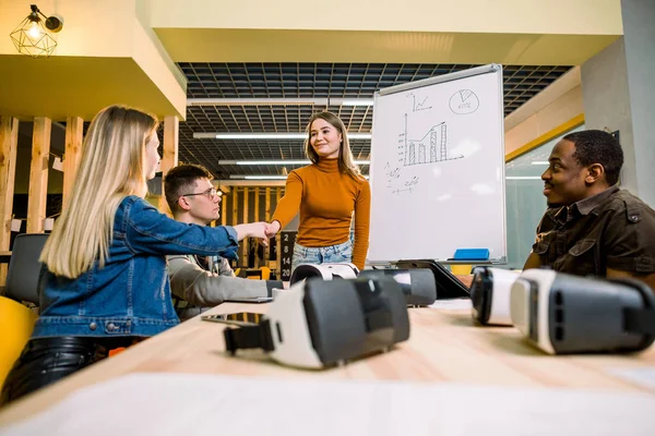 Multietnikus üzletemberek, akiknek csapatedzésen kell edzhetnek a VR szemüvegek alatt. Fiatal lány narancssárga pulóvert bemutató eredményeit a projekt munkatársakkal — Stock Fotó