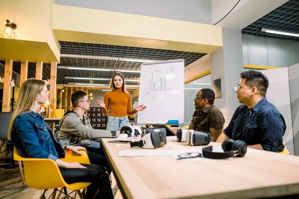 Gente de negocios multiétnicos teniendo ejercicio de entrenamiento en equipo durante el seminario con gafas VR. Chica joven en suéter naranja que presenta los resultados del proyecto para compañeros de trabajo —  Fotos de Stock