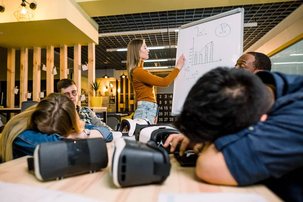 Equipo joven de personas multirraciales que duermen en la sala de conferencias durante una reunión. Jovencita dando un discurso cerca de la junta de la oficina. Después de un duro trabajo en la formación empresarial. Gafas VR sobre la mesa —  Fotos de Stock