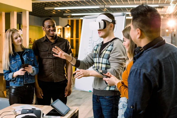 Équipe d'affaires de personnes multiraciales travaillant sur des applications et des jeux de réalité virtuelle, jeune homme excité testant des lunettes VR ou des lunettes debout dans la salle de bureau avec des collègues — Photo