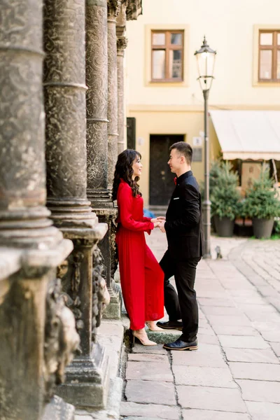 Šťastný a krásný čínský párek a žena se dívali jeden na druhého na pozadí starého města. Žena v červených šatech a muž v černém obleku — Stock fotografie