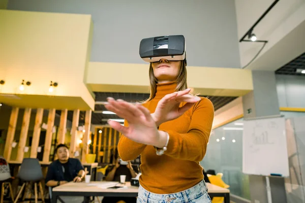 Kvinna i VR-headset som vidrör objekt i virtuell verklighet. Flicka interagerar med 3D-visualisering. Modernt IT-produkttest på digital Simulator koncept. Team av IT-arbetare på bakgrunden — Stockfoto