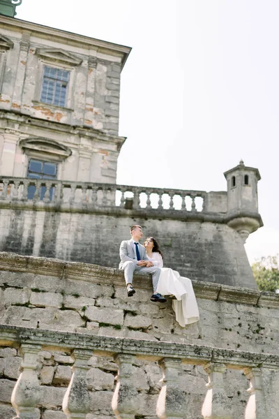 Krásný asijský svatební pár stojí při sezení na kamenné stěně starého zničeného hradu — Stock fotografie