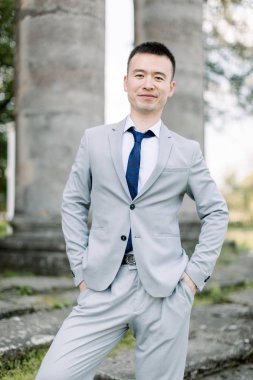 Eski kalede antik taş sütunların arka planda poz gri takım elbisezarif gülümseyen yakışıklı Asya damat