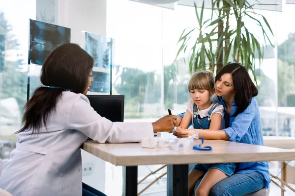 Medicina, cuidados de saúde e conceito de pediatria - médico afro-americano dando recomendações de tratamento para mãe caucasiana com filha bebê na clínica moderna — Fotografia de Stock