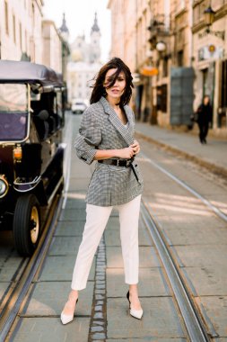 Genç güzel beyaz kız poz ve güneşli bir yaz gününde şehirde yürüyüş. Şehir yolunda duran ceket ve beyaz pantolon giyen kısa koyu saçlı pretty kadın