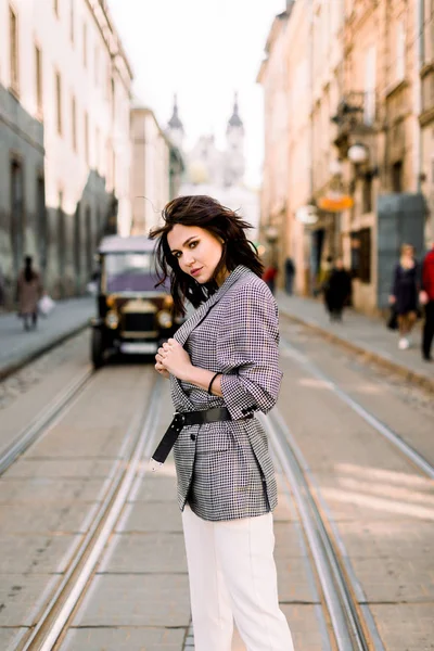 Attraente donna moderna in piedi sulla strada della città. Bella donna elegante su una strada di città, auto retrò sullo sfondo — Foto Stock