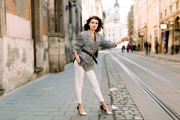 Immagine di donna bruna in abiti da lavoro alla moda che ferma taxi o auto nella strada della città — Foto Stock