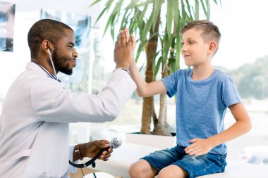 Mutlu gülümseyen Afrikalı Amerikalı erkek doktor modern tıp kliniğinde küçük bir çocuk beş veren. Tıbbi muayene iyi