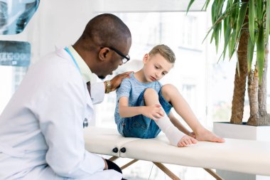 Düştükten sonra çocuk. Koyu tenli hoş çocuk doktoru düştükten sonra çocuğun elastik bandaj bacak bakıyor