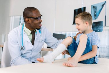 hastanede küçük hasta çocuğun elastik bandaj ile bacak inceleyen afrikalı-Amerikalı doktor yan görünümü