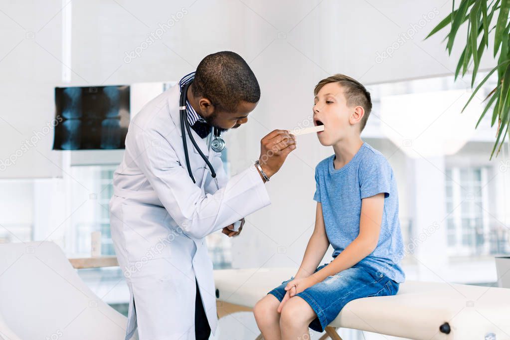 Showing throat. Little boy opening mouth showing her throat while visiting young handsome African man doctor in his medical office